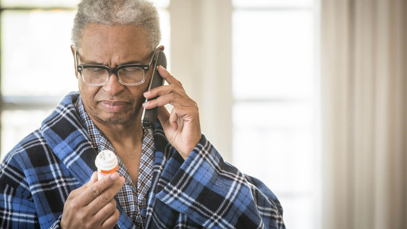 elderly man reading prescription bottle while on the phone