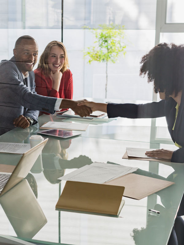 Photograph of businesspeople at a glass table, two shaking hands while another smiles