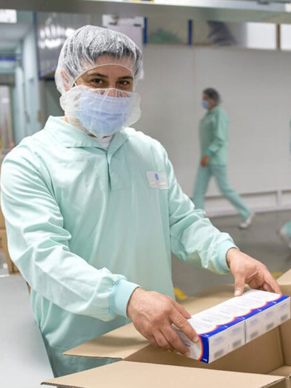Worker in protective clothing packing a product box in a sterile facility.