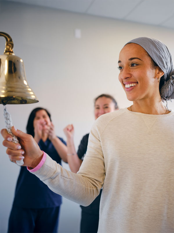 Photograph of a woman ringing a brass bell as people cheer in the background