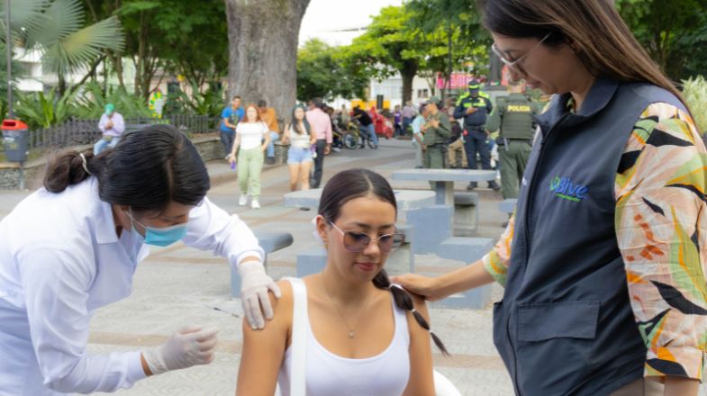 Photograph of a woman receiving a vaccine shot outdoors while another woman comforts her