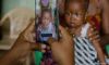 Hands holding a smartphone, photographing a woman in patterned clothing holding a baby