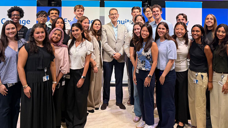 Photograph of a smiling group of young adults posing with a suited man indoors thumbnail
