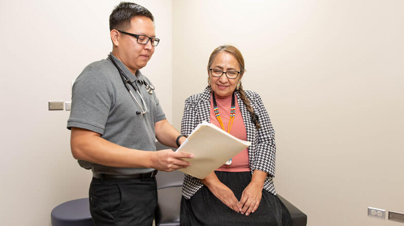 Photograph of a doctor showing a medical file to a smiling patient in an exam room thumbnail
