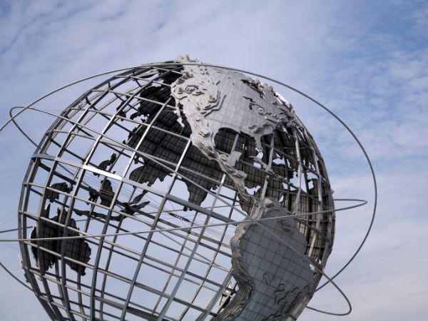 Photograph of a metal globe sculpture against a partly cloudy sky