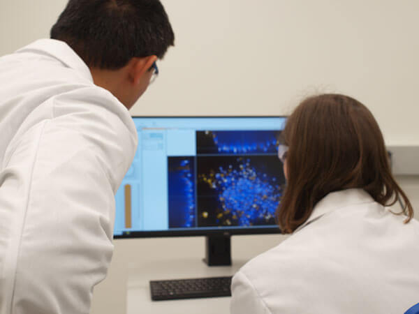 Photograph of two scientists in lab coats analyzing data on a monitor