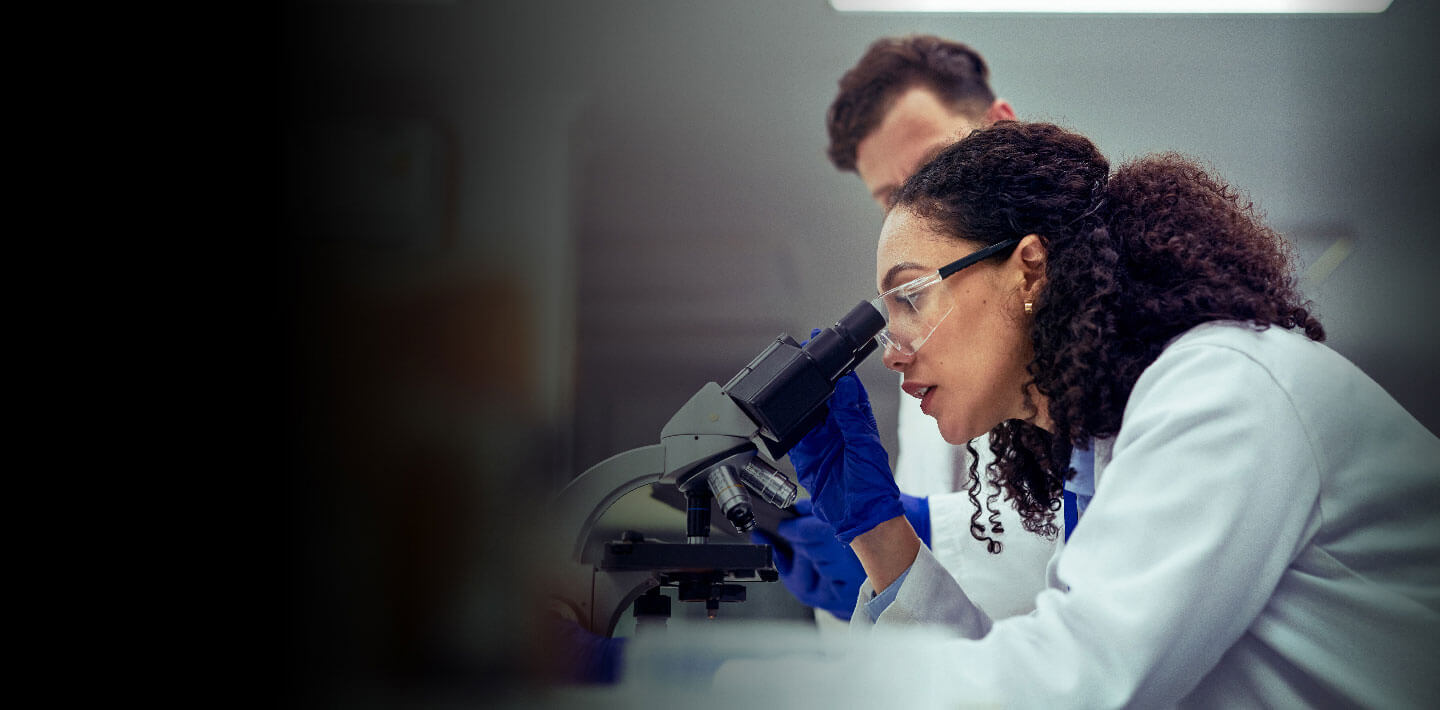 Joshs Story homepage banner, scientist looking through microscope