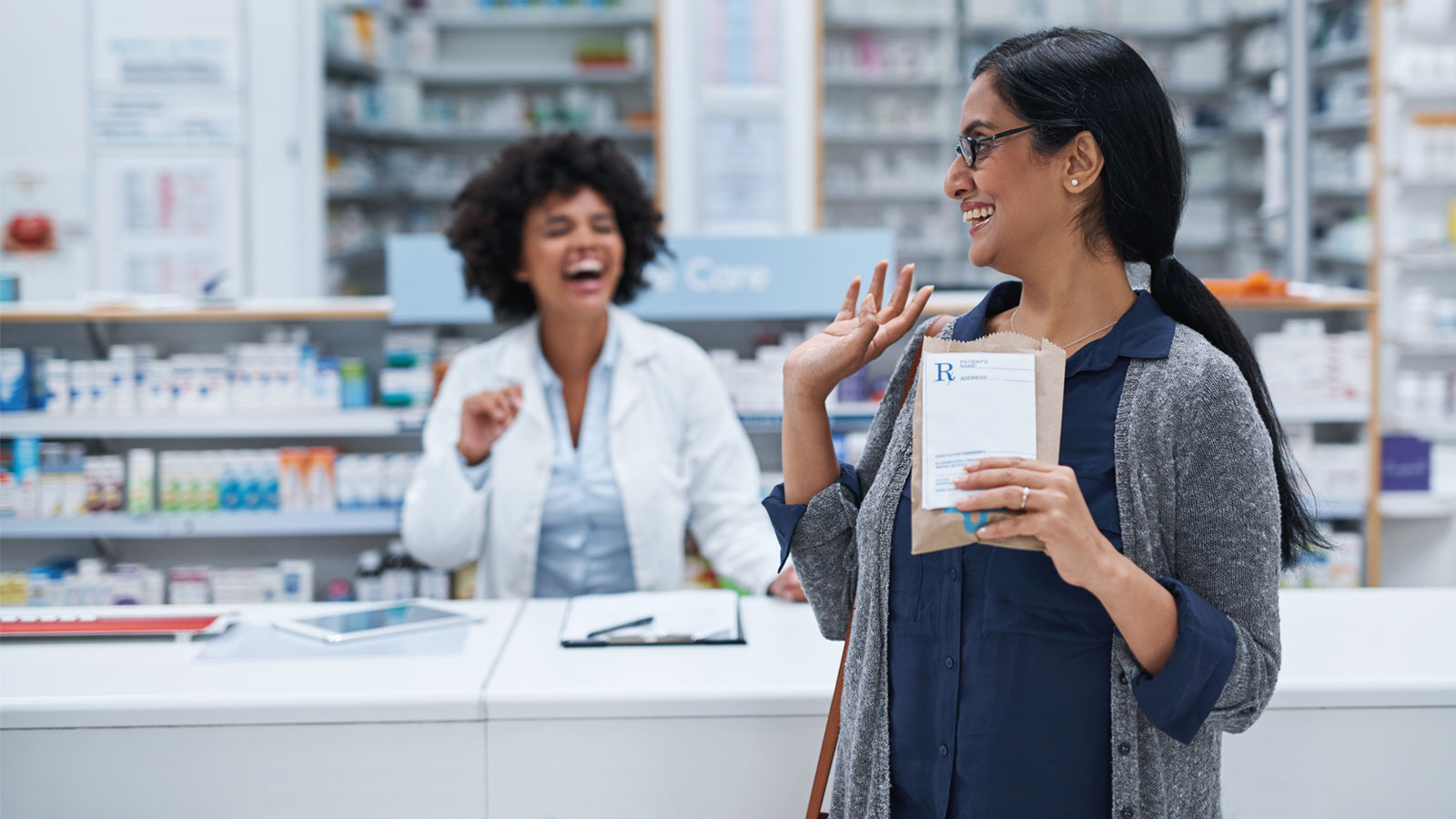 Shot of a mature woman waving to a pharmacist in a chemist