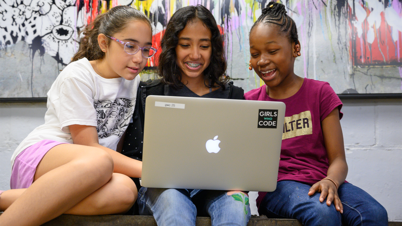 three young girls students viewing a laptop computer.