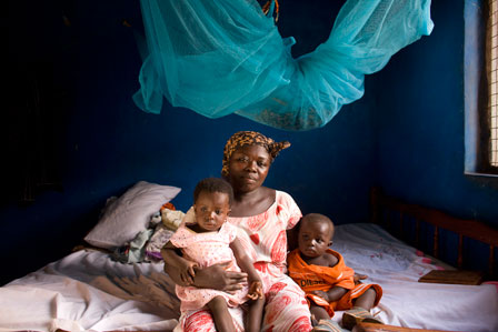 A mother sits with her two children beneath the mosquito net. The MAM program aims to educate communities about the causes of malaria and encourages mothers to seek prompt and effective treatment with ACTs.