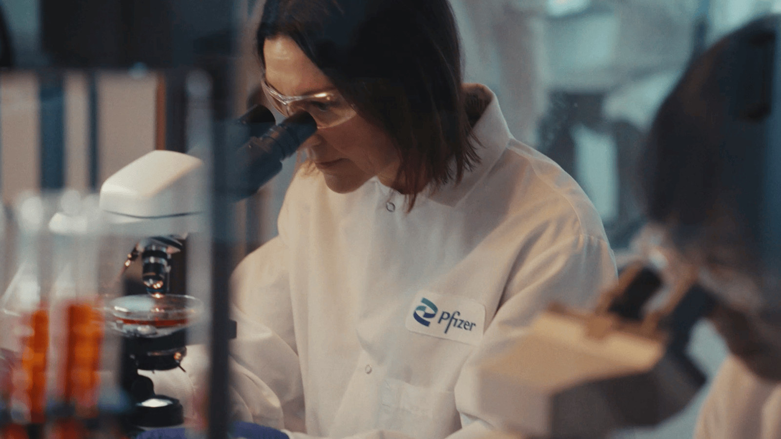Photograph of a lab technician in a white coat working at a microscope