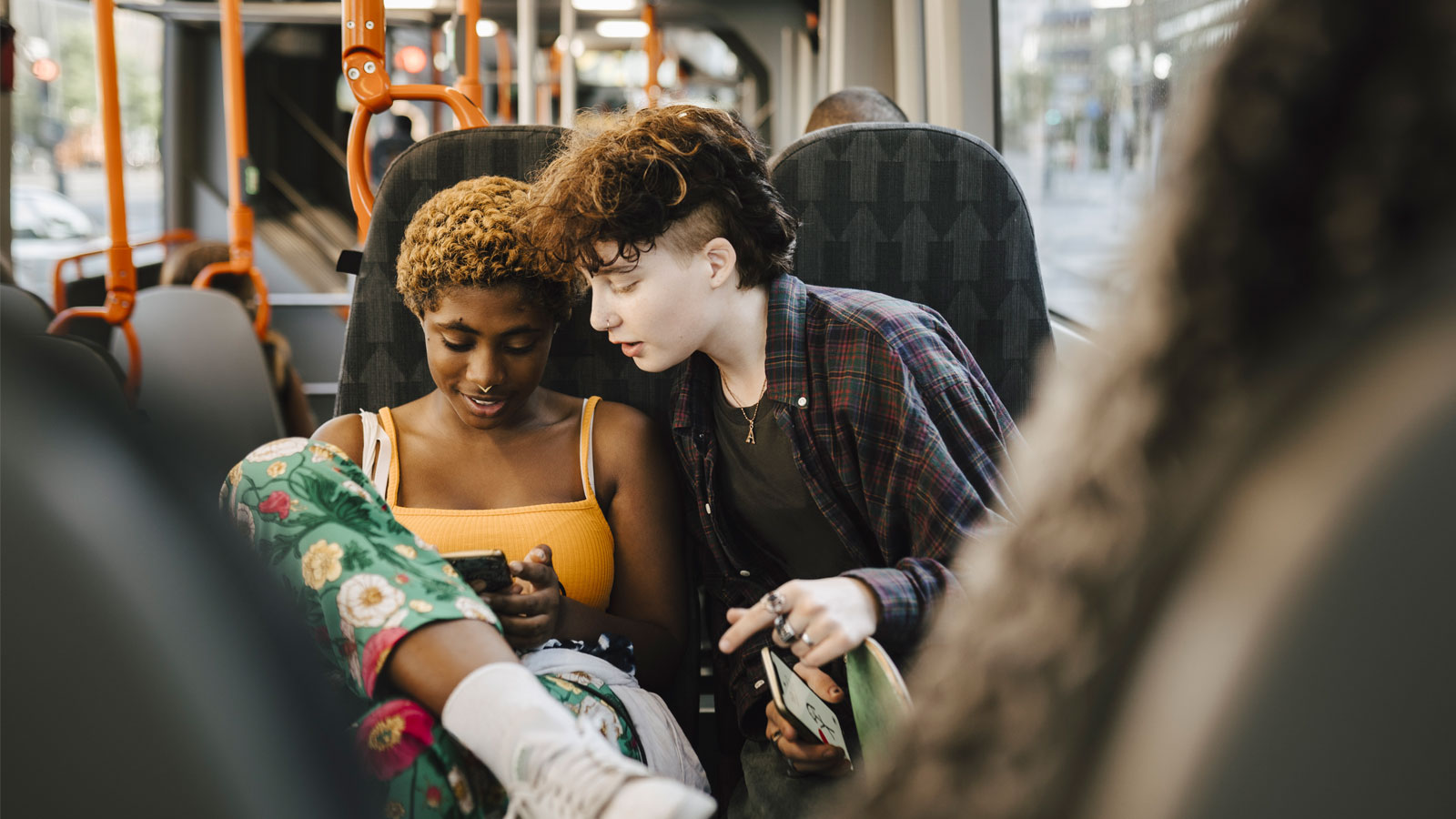 Teenage boy looking at young non-binary woman using smart phone in bus