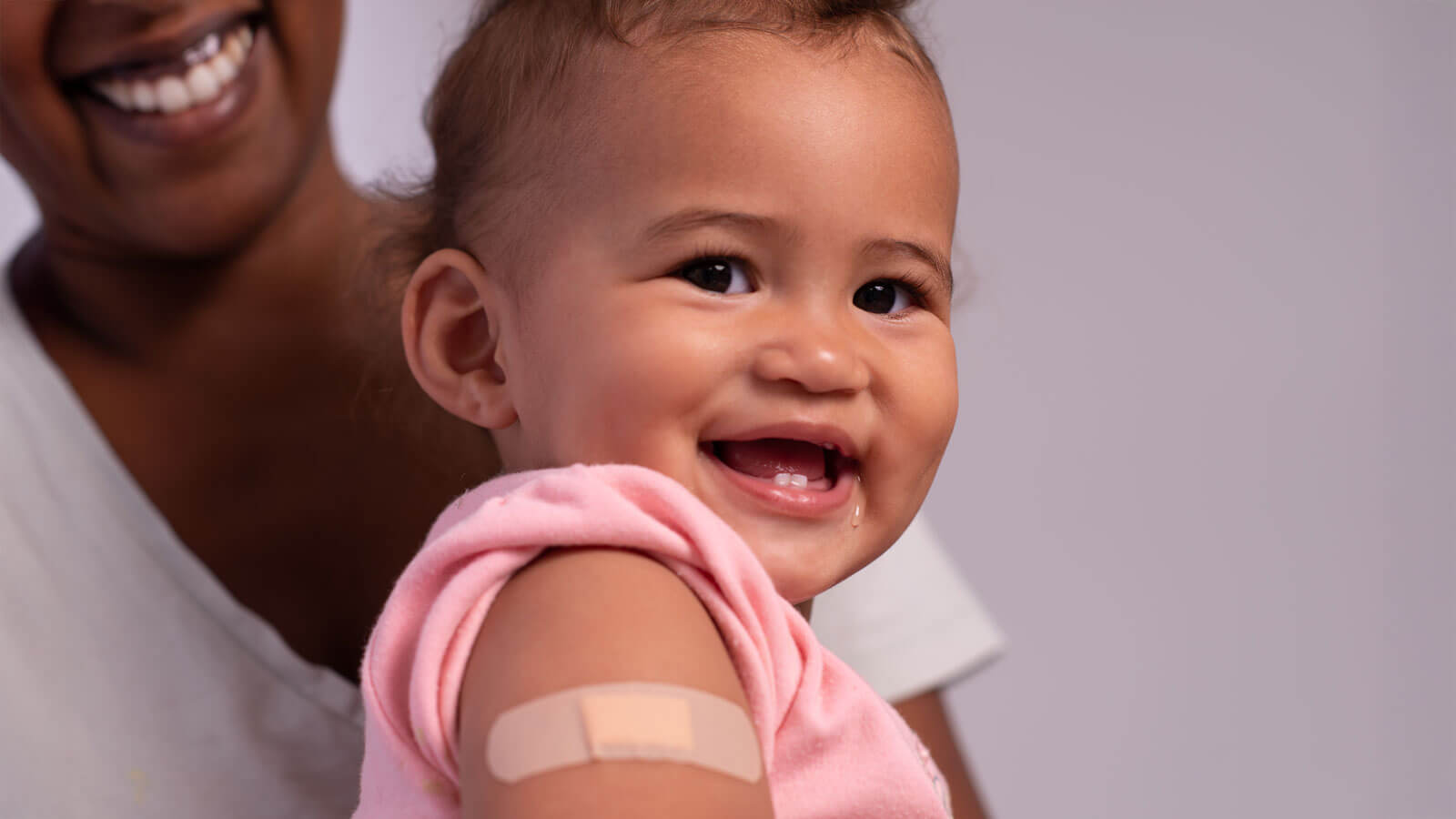 An adhesive bandage on an upper arm with the smile. Baby girl with band-aid patch on her upper arm.