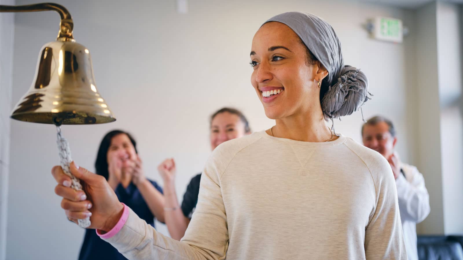 An adult woman chemotherapy patient in a treatment office, celebrating the completion of her treatment with a ceremonial bell ring.