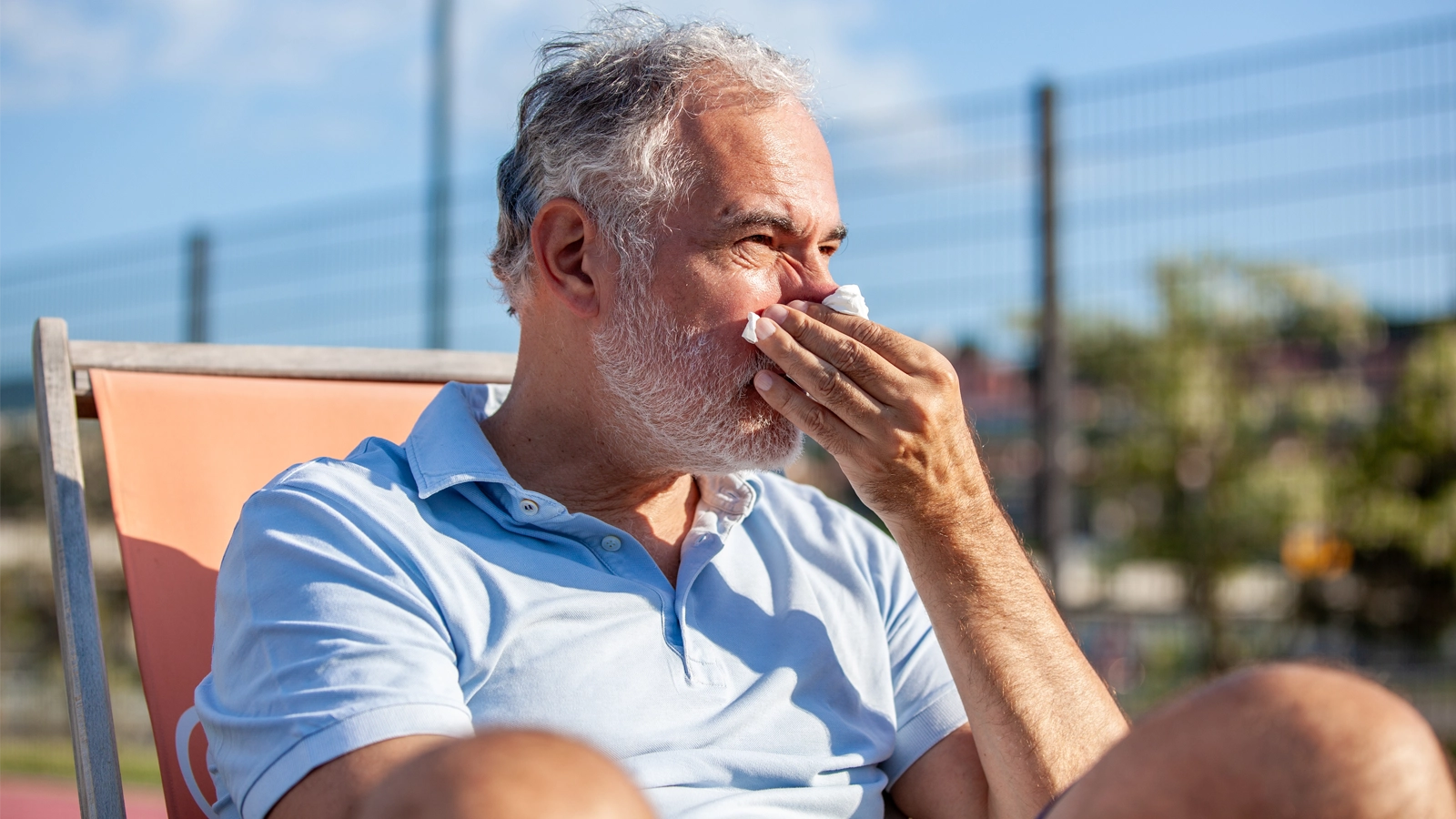 man sitting down blowing his nose