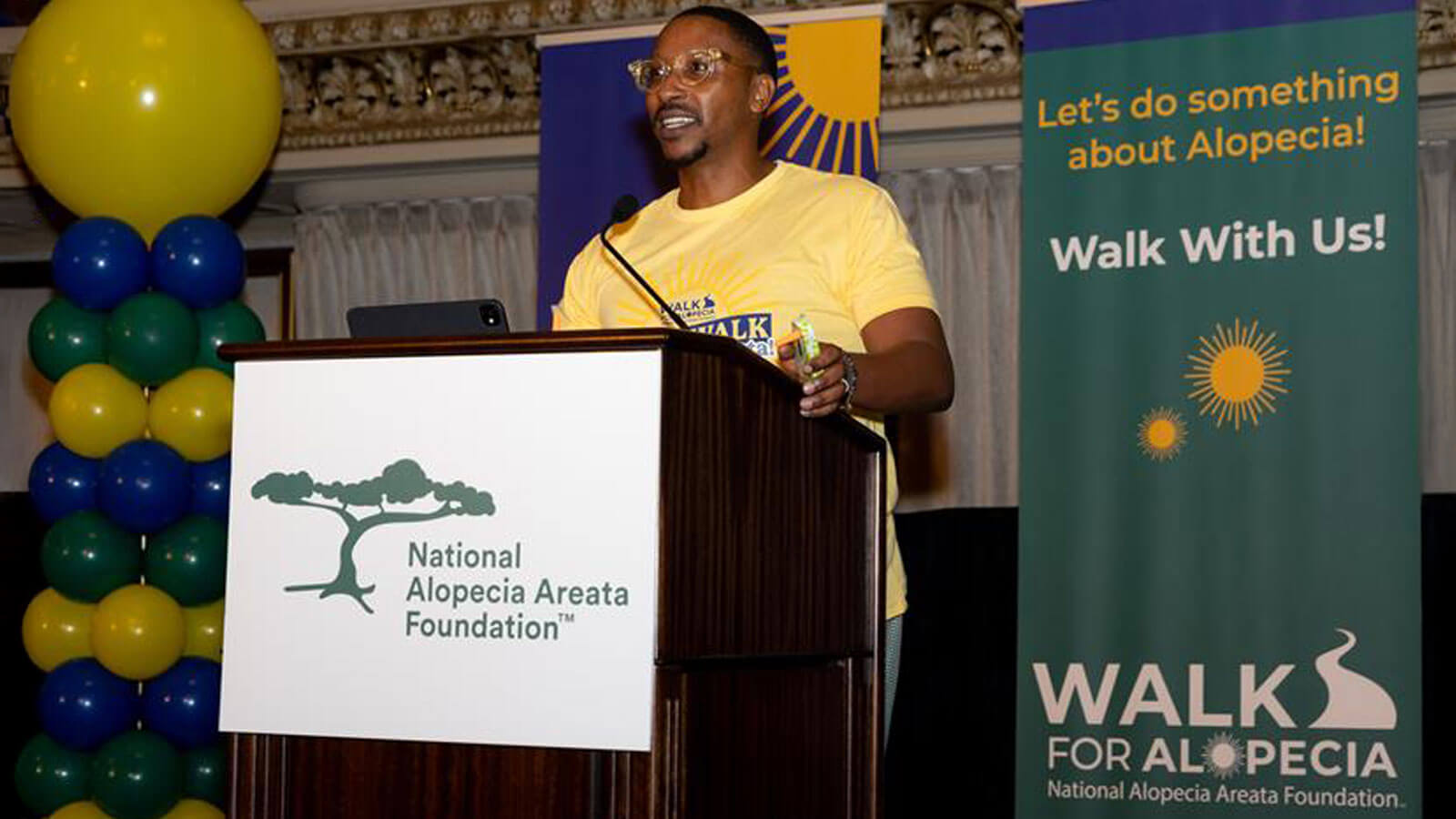 Tyrone speaking in front of podium at National Alopecia Areata Foundation Walk for Alopecia Areata