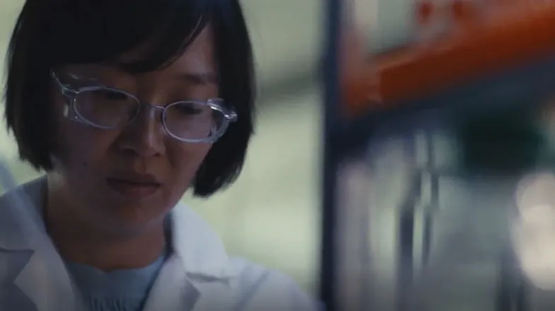 Scientist in a lab coat working beside blurred laboratory equipment thumbnail