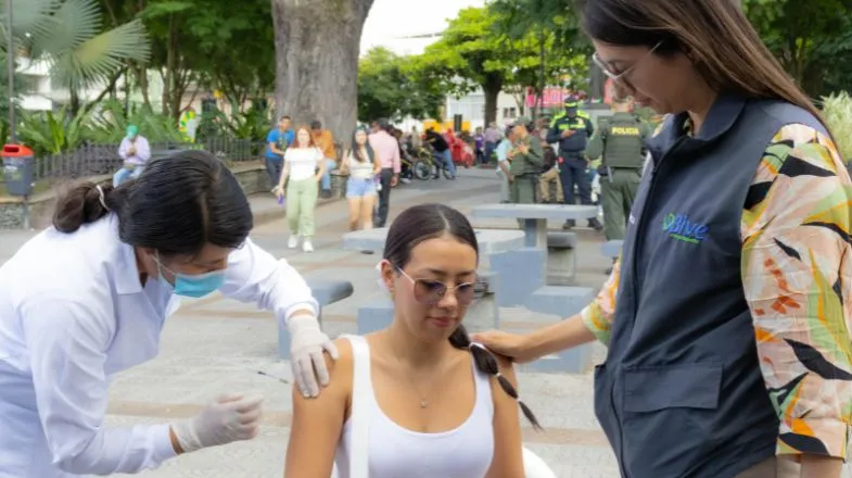 Photograph of a woman receiving a vaccine shot outdoors while another woman comforts her