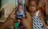 Hands holding a smartphone, photographing a woman in patterned clothing holding a baby