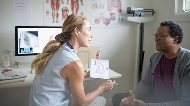 Photograph of a doctor explaining a medical diagram to a seated patient in an exam room thumbnail