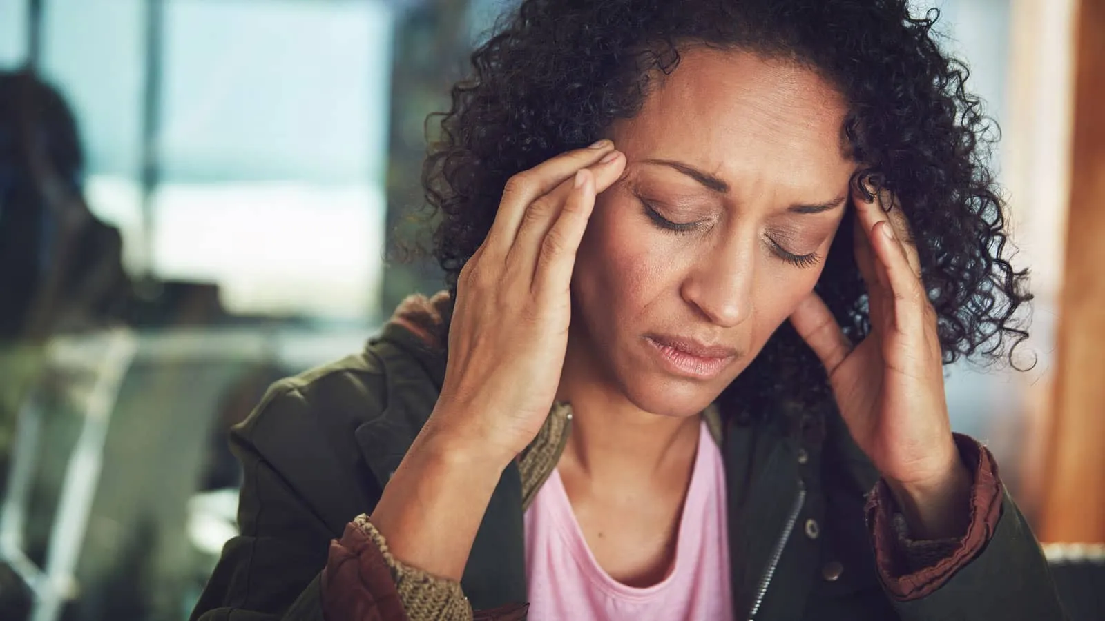 Photograph of a person indoors holding their head with both hands, looking stressed