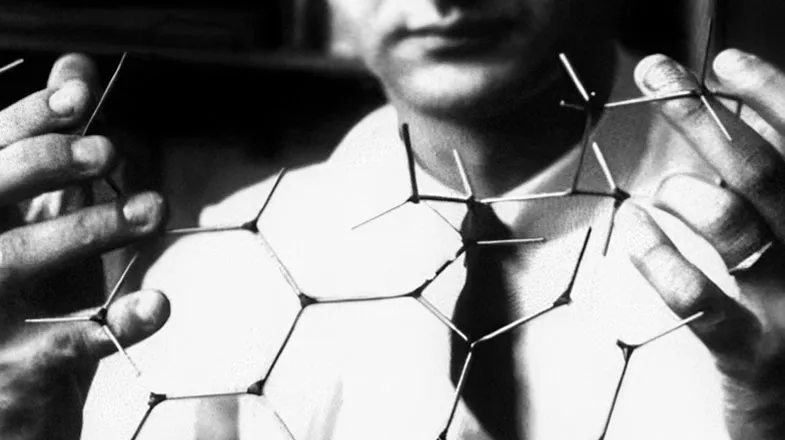 Black-and-white photo of a scientist holding a wireframe molecular model
