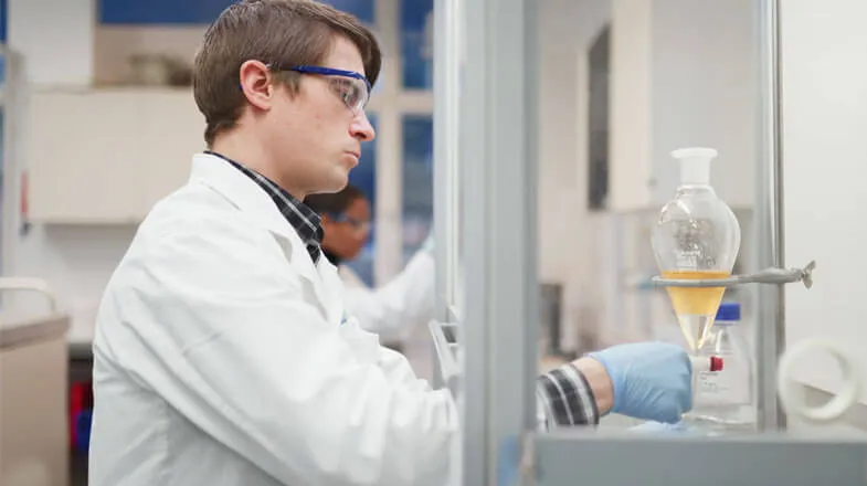 Photograph of a scientist in a lab coat working with glassware in a laboratory thumbnail