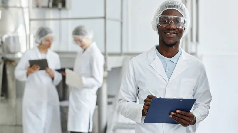 Photograph of smiling lab worker with clipboard; two colleagues work in background thumbnail