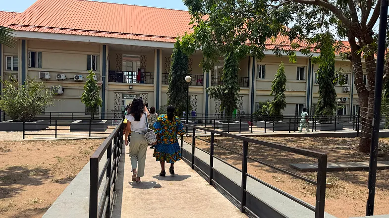 People walking up a ramp toward a large tan building with trees and a red roof
