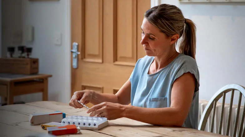 Photograph of a woman at a kitchen table organizing pills in a pillbox