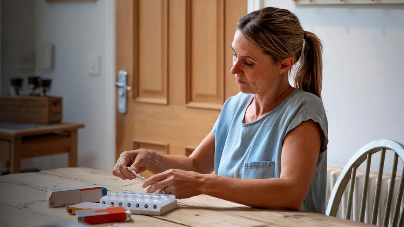 Photograph of a woman at a kitchen table organizing pills in a pillbox