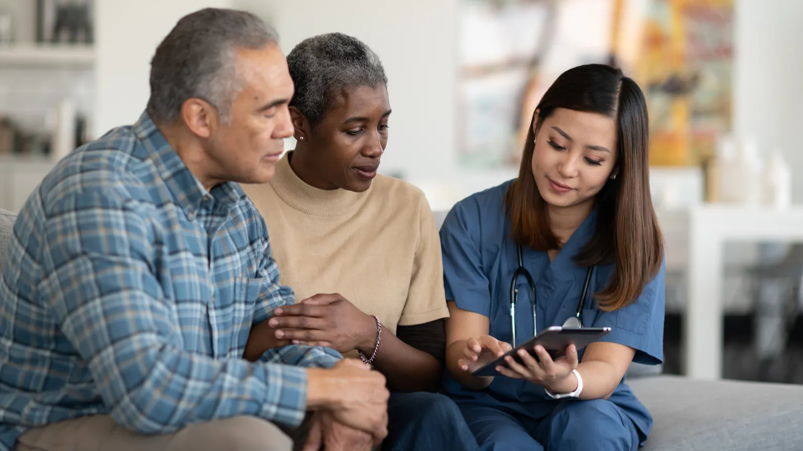 Female healthcare worker showing a tablet to an older couple on a couch