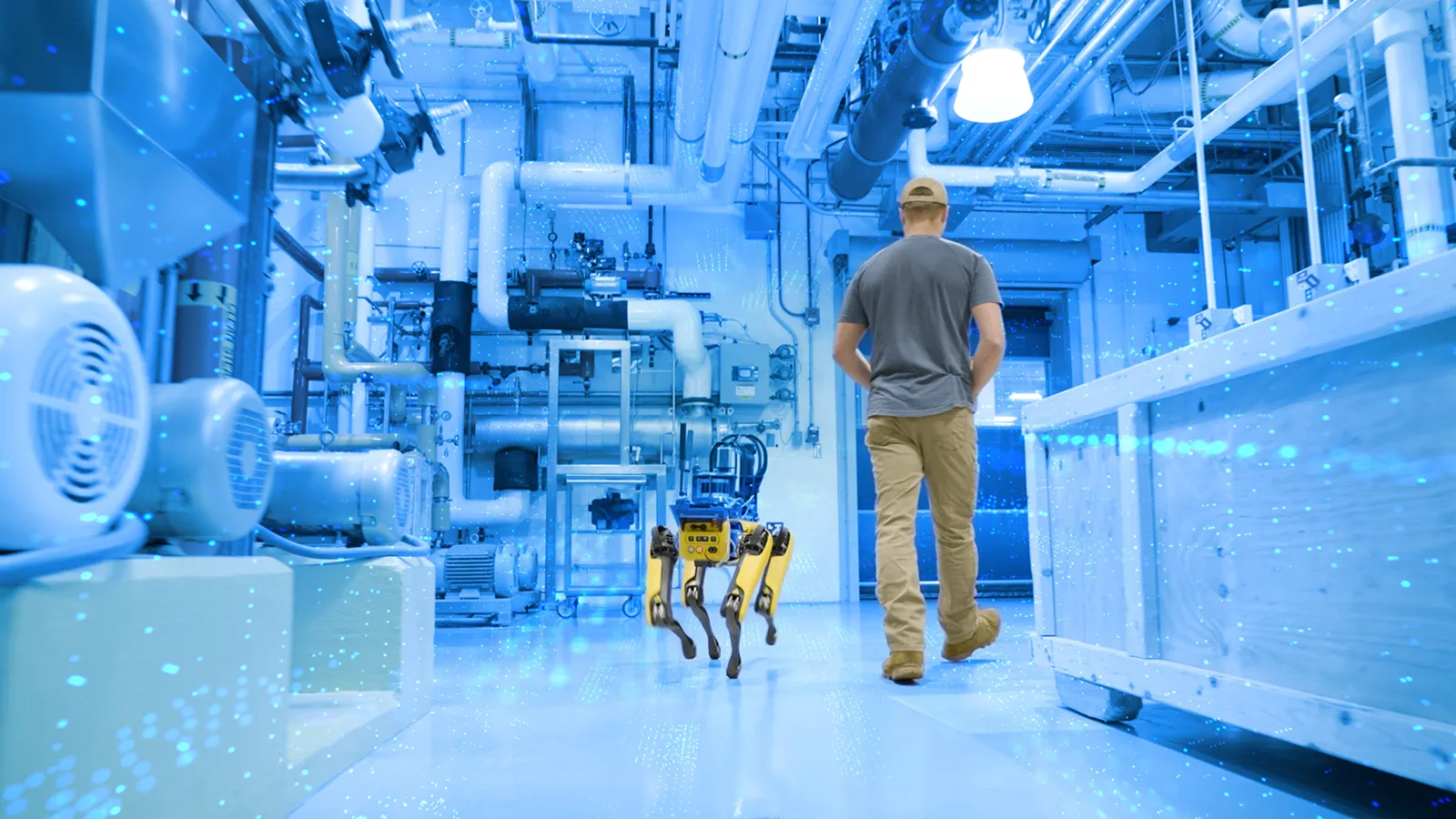 Photograph of a worker and a yellow robot dog walking through a blue-lit industrial plant