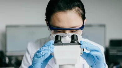 lab technician looking through microscope lens
