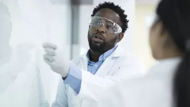 lab technician writing on an eraser board while colleague watches
