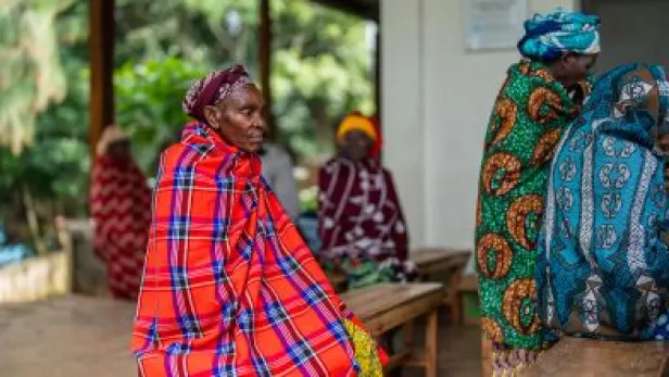 Photograph of women in colorful patterned wraps sitting and talking on wooden benches