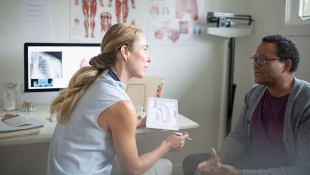 Photograph of a doctor explaining a medical diagram to a seated patient in an exam room thumbnail