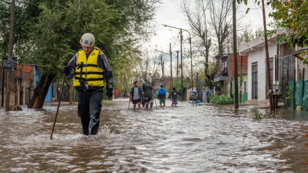 Photograph of people wading through a flooded residential street in rain gear