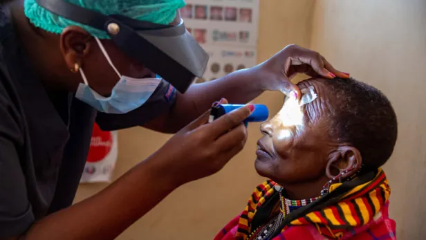 Photograph of a clinician examining an older woman’s eye with a bright handheld light