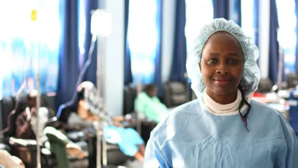 Smiling medical worker in scrubs and cap standing in a busy hospital ward