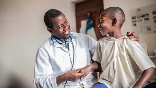 Photograph of a smiling doctor comforting a young boy in a clinic.