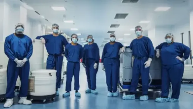 Photograph of masked medical staff in blue scrubs standing in a hospital corridor