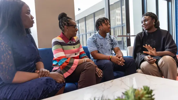 Photograph of four people sitting on a couch, talking and smiling in a bright room