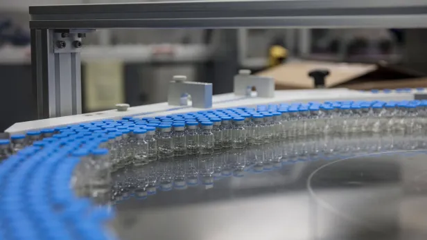 Photograph of a pfizer factory conveyor lined with small glass vials and blue caps