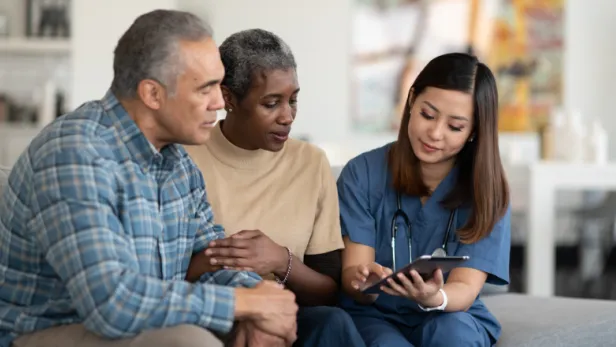 Female healthcare worker showing a tablet to an older couple on a couch