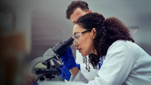 Photograph of a scientist using a microscope, with a colleague standing behind thumbnail