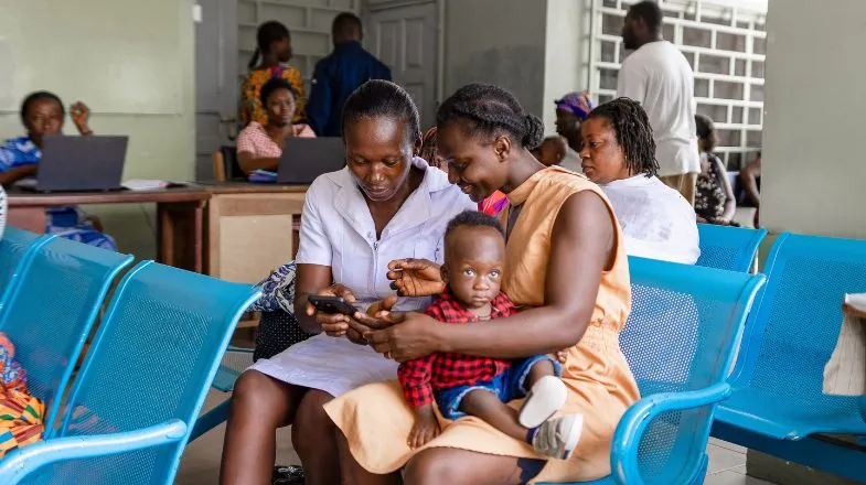Photograph of a woman and mother smiling at a phone while a baby sits on the mother’s lap